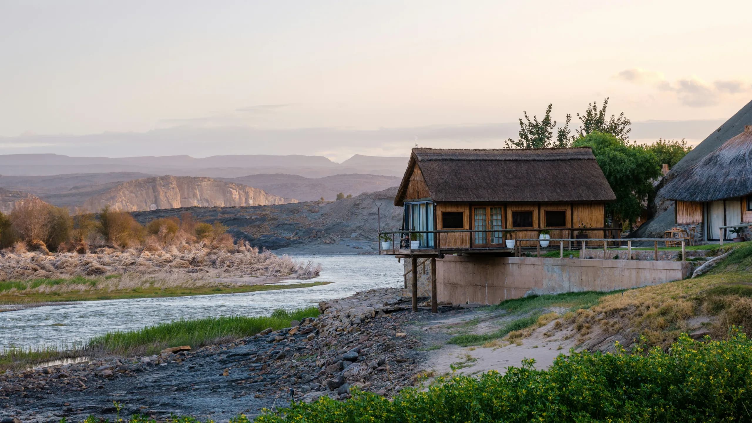 Thatched lodges beside an African river at dusk